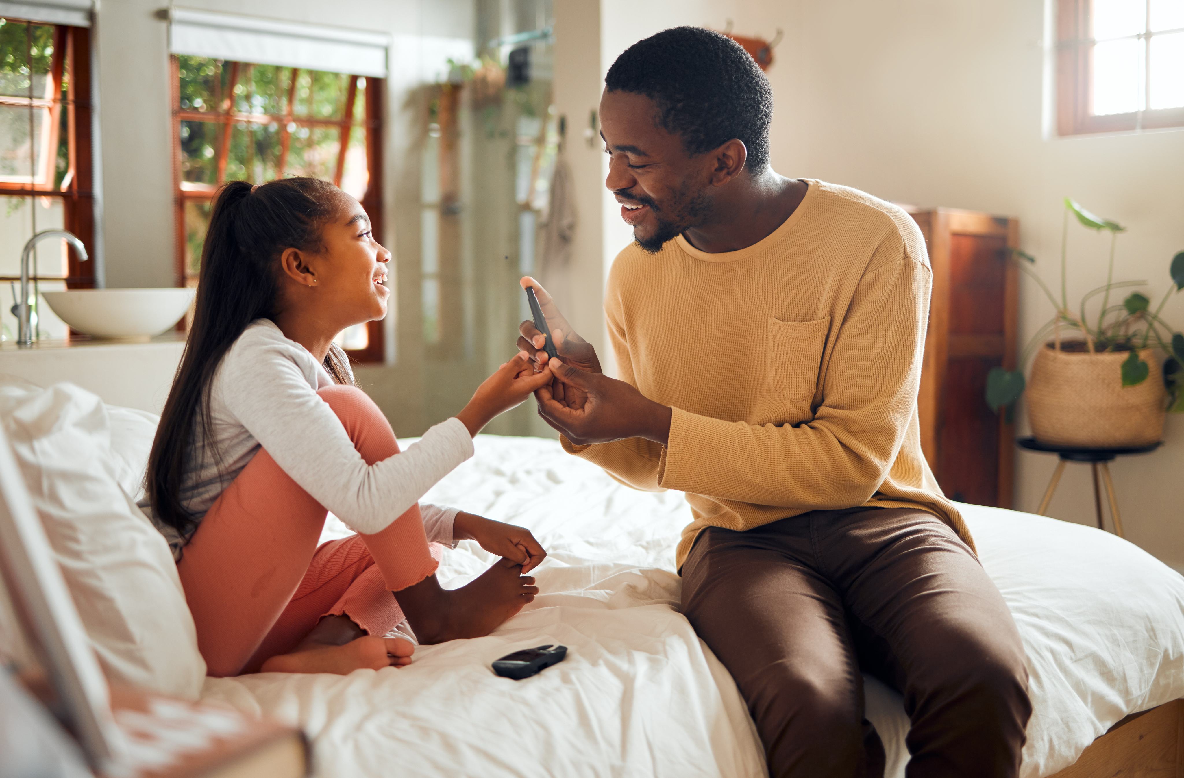 A father helping his daughter check her blood glucose.